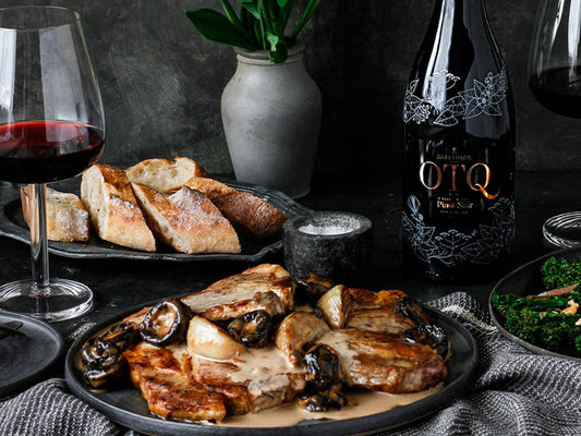 A plate of pork and prunes, served with baguette and a bottle of On The Quiet Pinot Noir