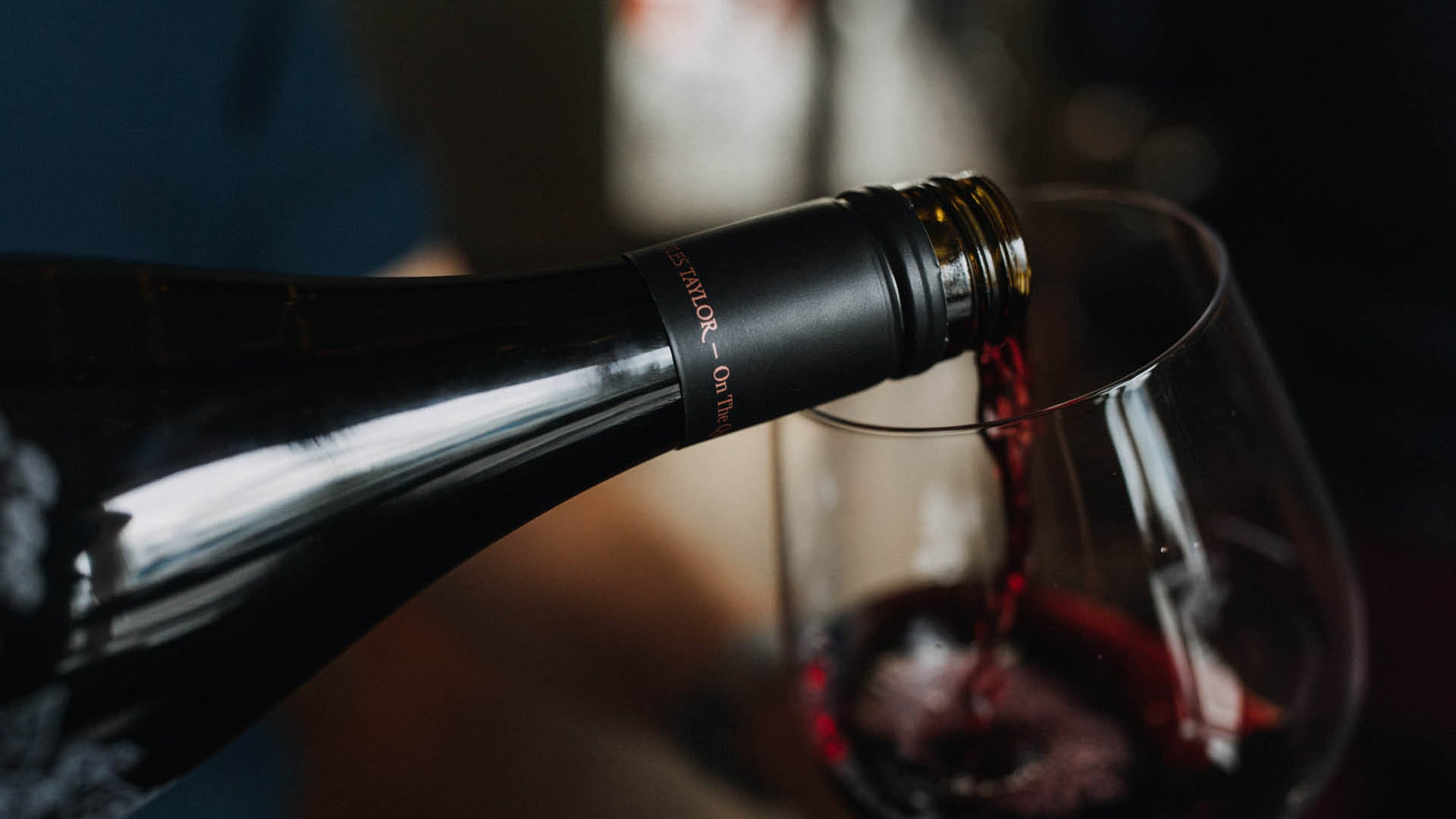 Pinot Noir wine being poured from an On The Quiet bottle into a wine glass, with a softly blurred background.