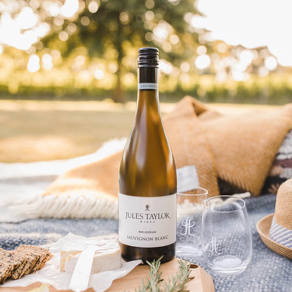 Bottle of Jules Taylor Sauvignon Blanc with a glass on a picnic blanket outdoors.